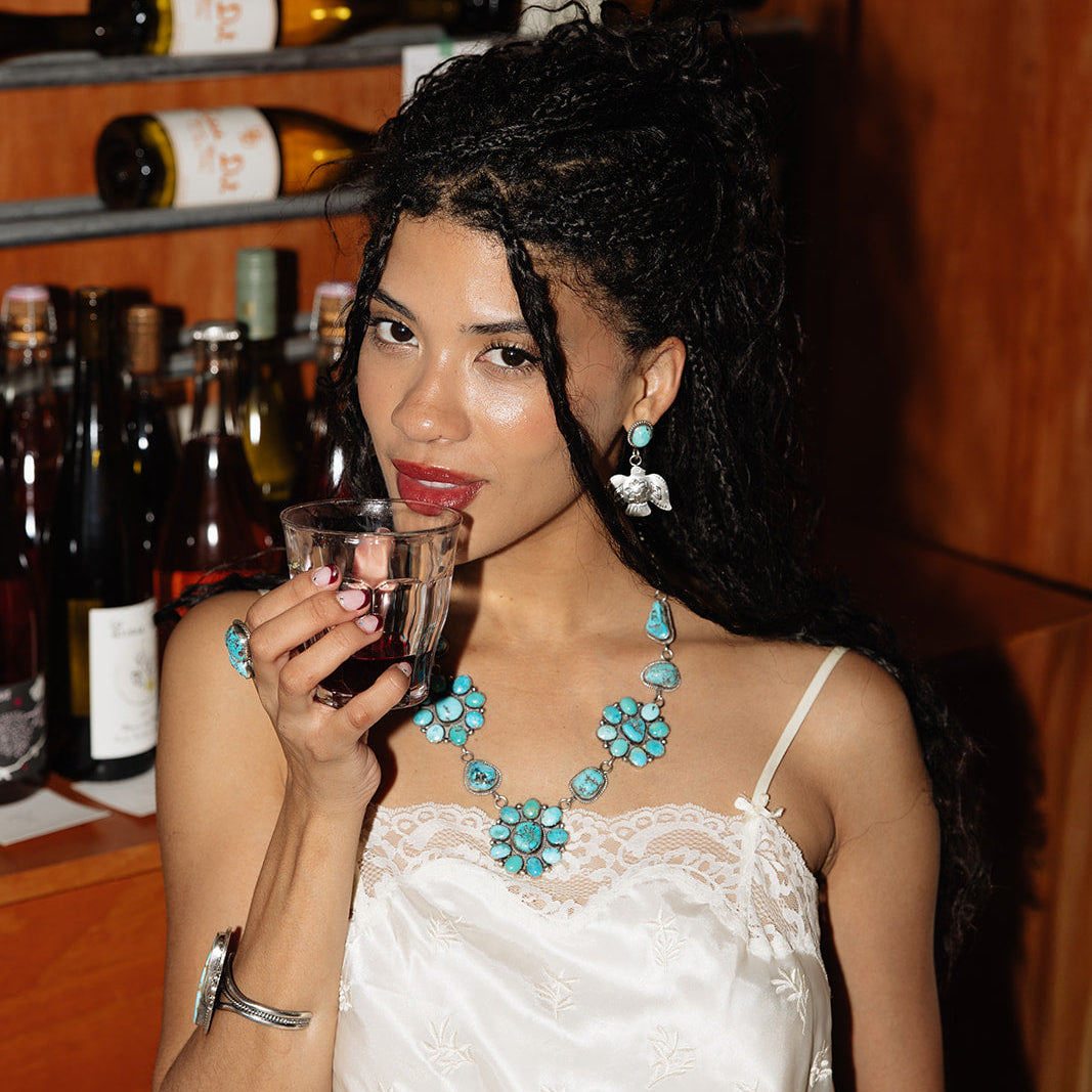 Woman drinking from a glass with wine bottles in the background
