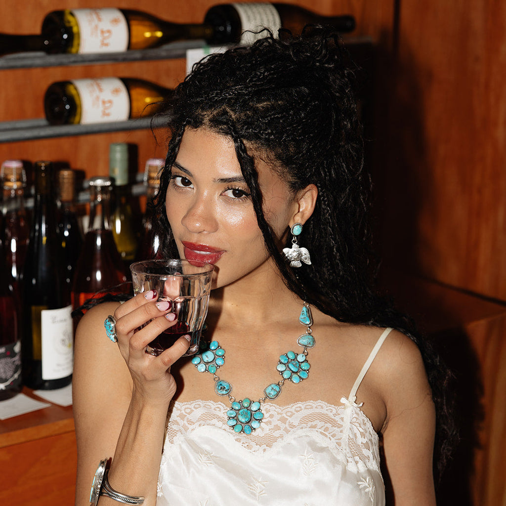Woman drinking from a glass with wine bottles in the background