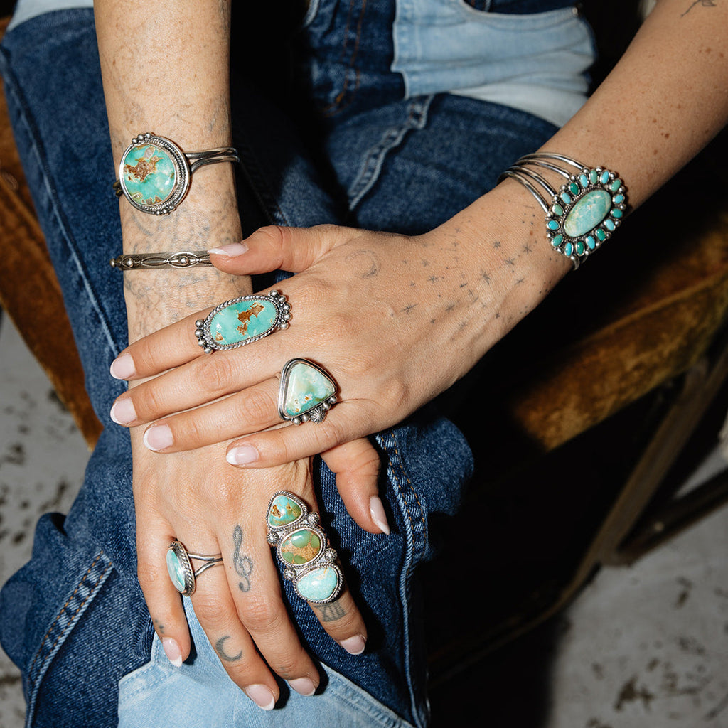 Person wearing multiple turquoise rings on a blurred background