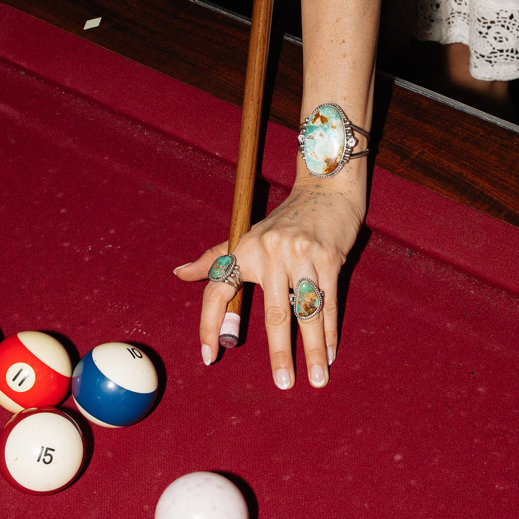 Hand with multiple rings on a pool table with pool balls