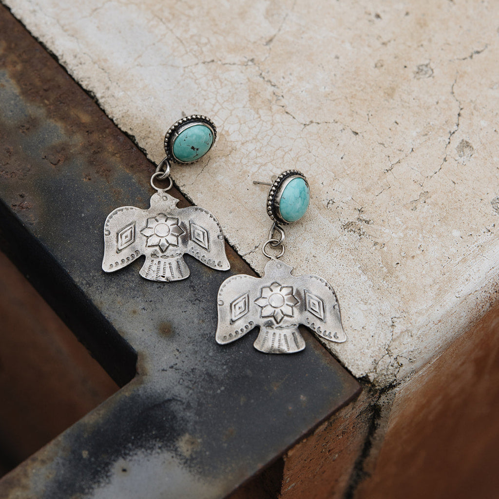Silver earrings with turquoise stones on a textured surface