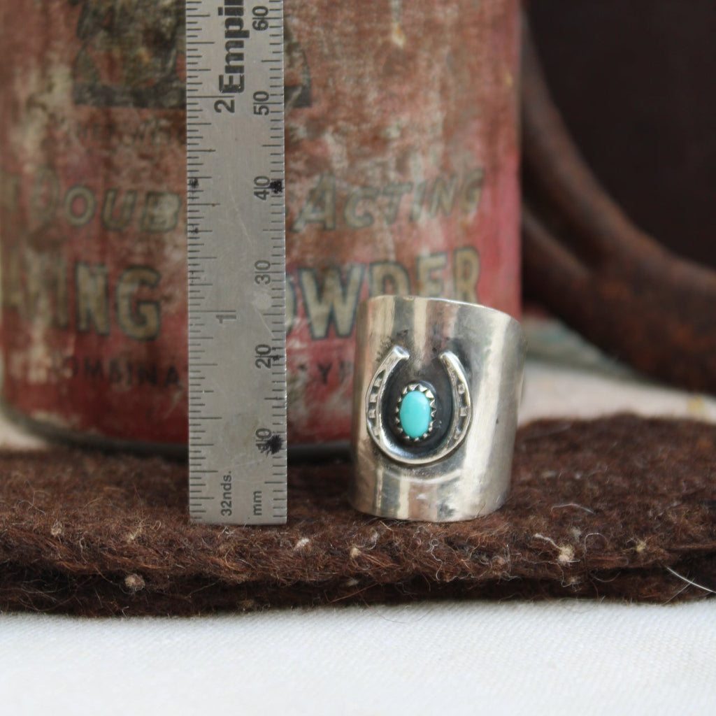 Close-up of a cylindrical metal object with a turquoise stone, placed on a textured surface with a ruler for scale.