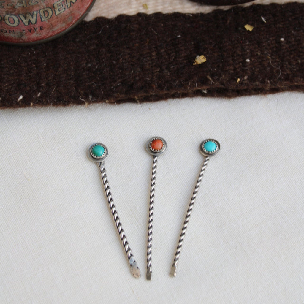 Three silver hairpins with gemstones on a textured surface