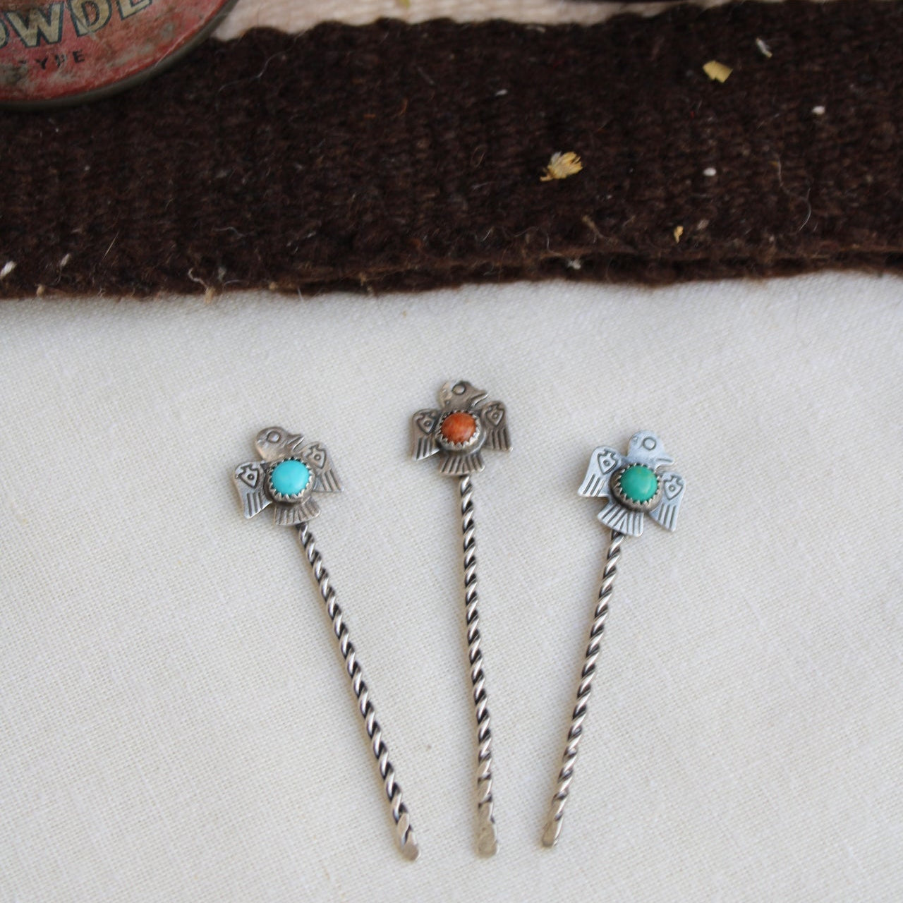 Three silver hairpins with gemstones on a textured surface