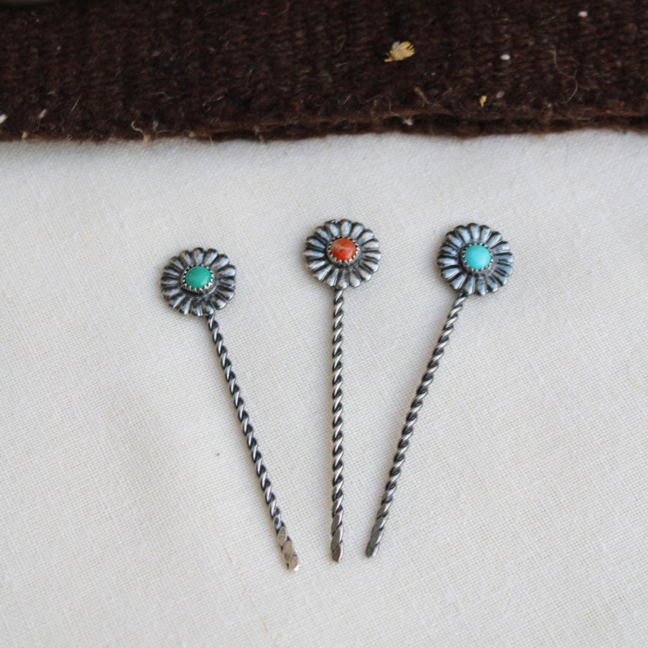 Three decorative hair pins with floral designs on a textured surface.