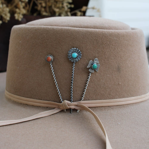 Turquoise and silver hairpins on a beige hat with a blurred background