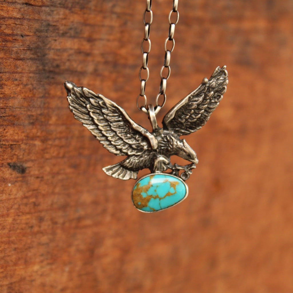 A sterling silver eagle pendant necklace holding a turquoise stone, resting on a rustic wooden surface.