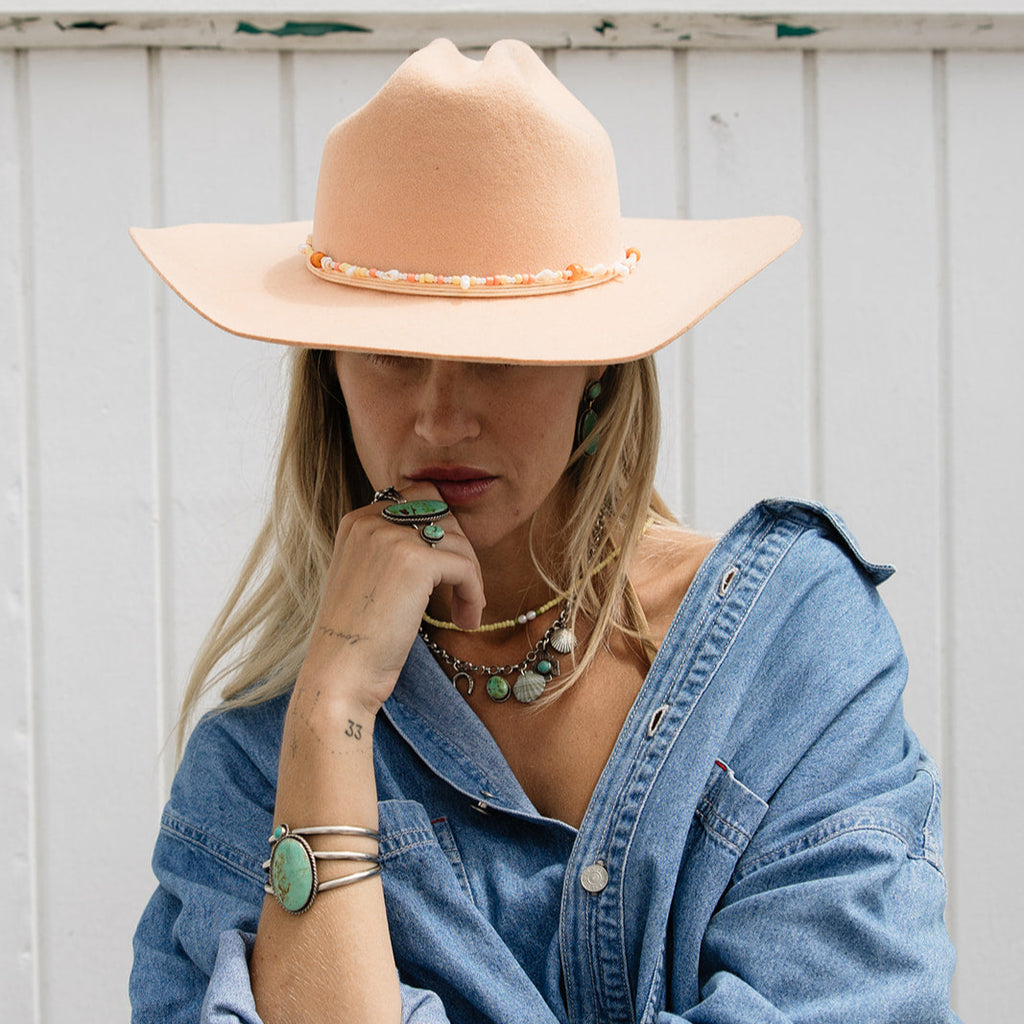 Woman wearing a wide-brimmed beige hat and denim shirt against a white wooden background