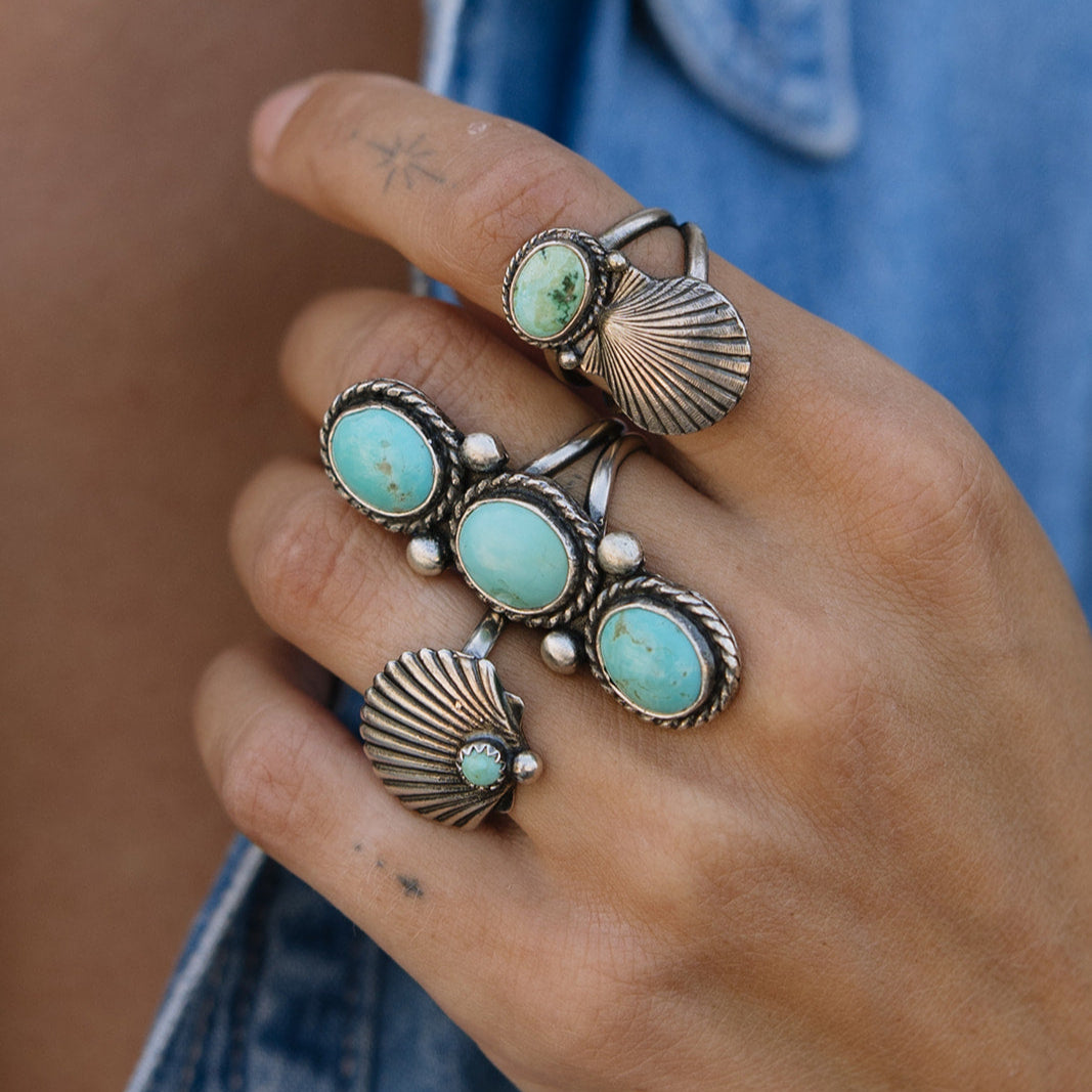 Close-up of a hand wearing multiple turquoise stone rings with silver bands.