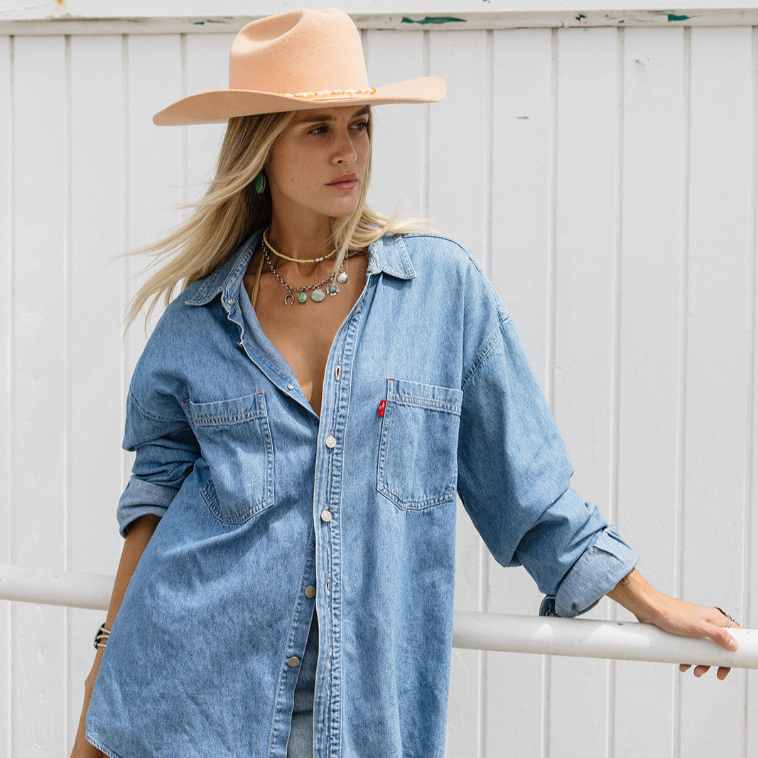 Woman wearing a denim shirt and beige hat against a white wooden background