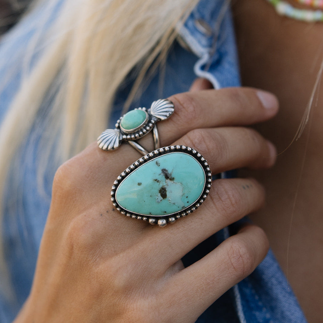 Close-up of a hand wearing two turquoise rings with a denim jacket background