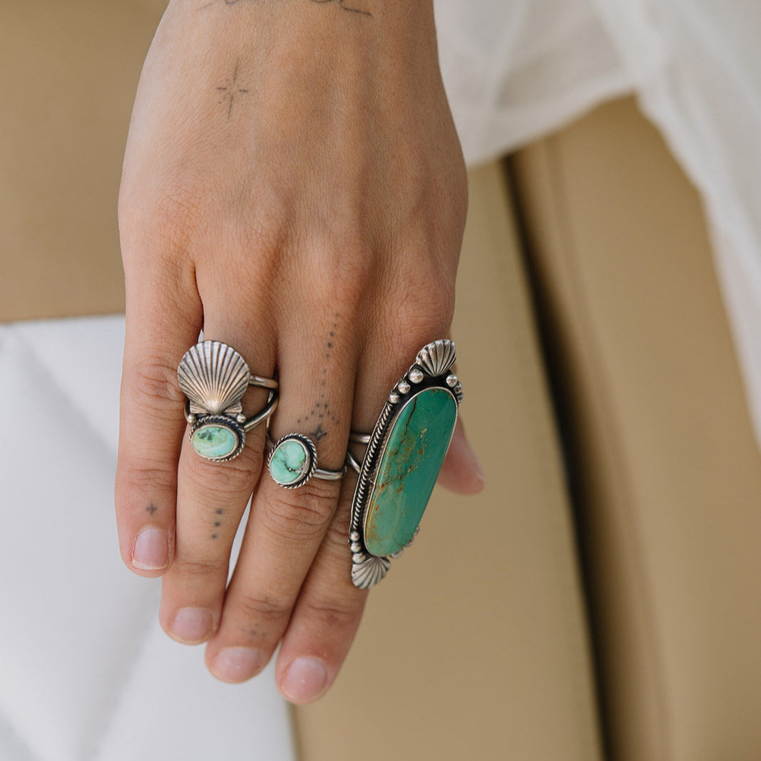 Hand wearing multiple rings with turquoise stones and silver bands on a neutral background