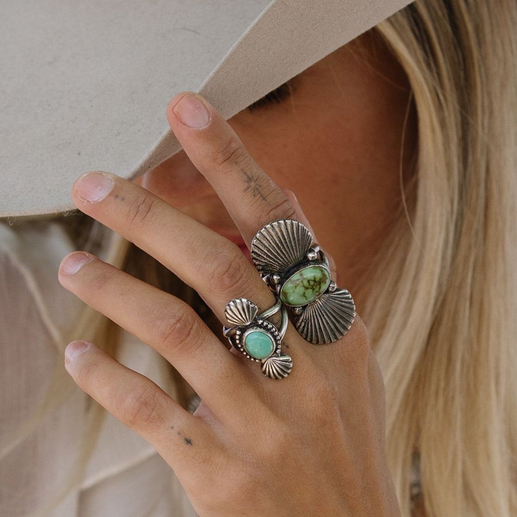 Close-up of a hand wearing multiple rings with turquoise stones and silver bands, holding a beige hat.