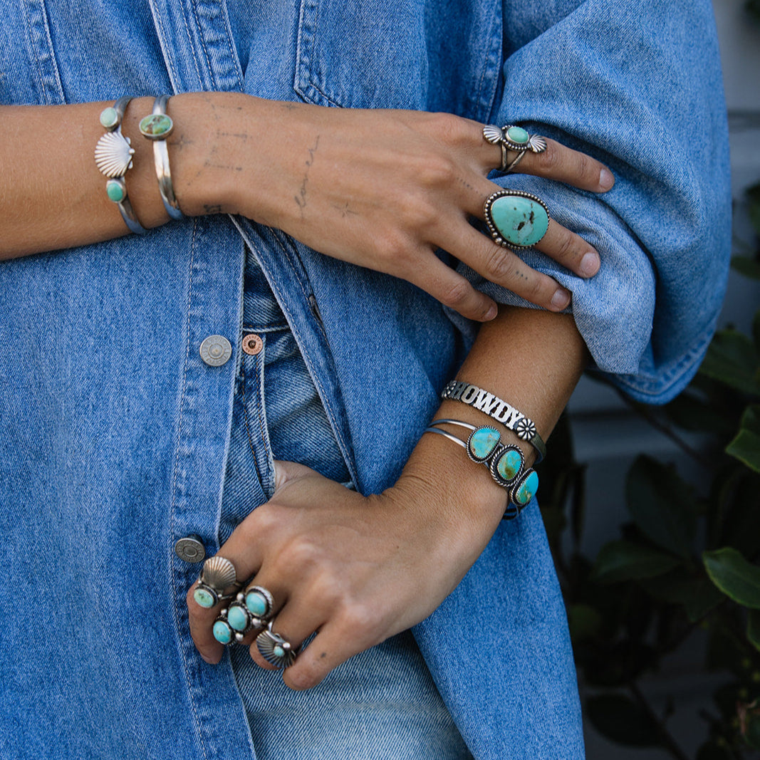 Person wearing a blue denim jacket with turquoise jewelry on hands and wrists.