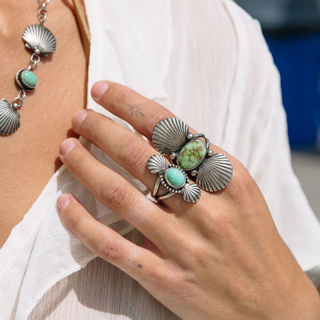 Close-up of a hand wearing a silver ring with turquoise stones, with a blurred background.