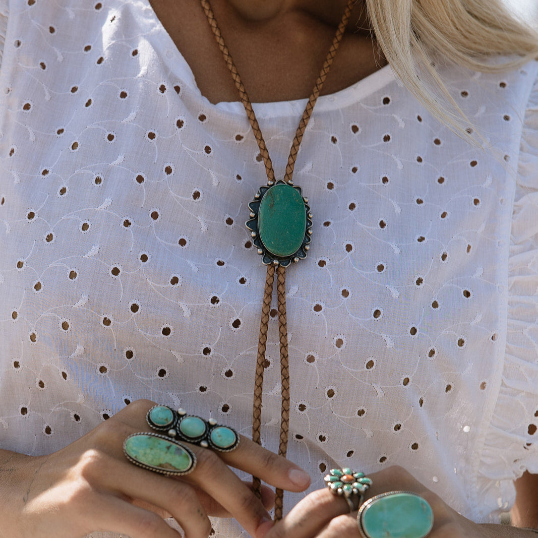 Person wearing turquoise jewelry including a necklace, ring, and earrings on a white polka dot shirt.