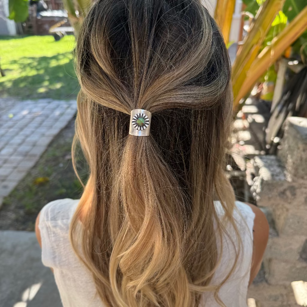 Person with a hair clip in their hair, standing outdoors with plants and steps in the background